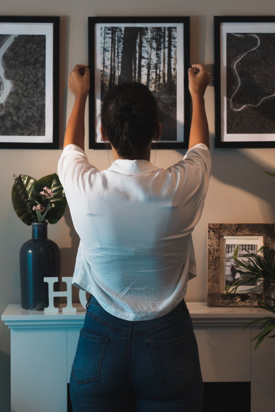 Afbeelding: Iemand hangt een ingelijste foto aan de muur als voorbeeld van de waarde van geprinte foto's na het maken van een foto met een creatieve techniek