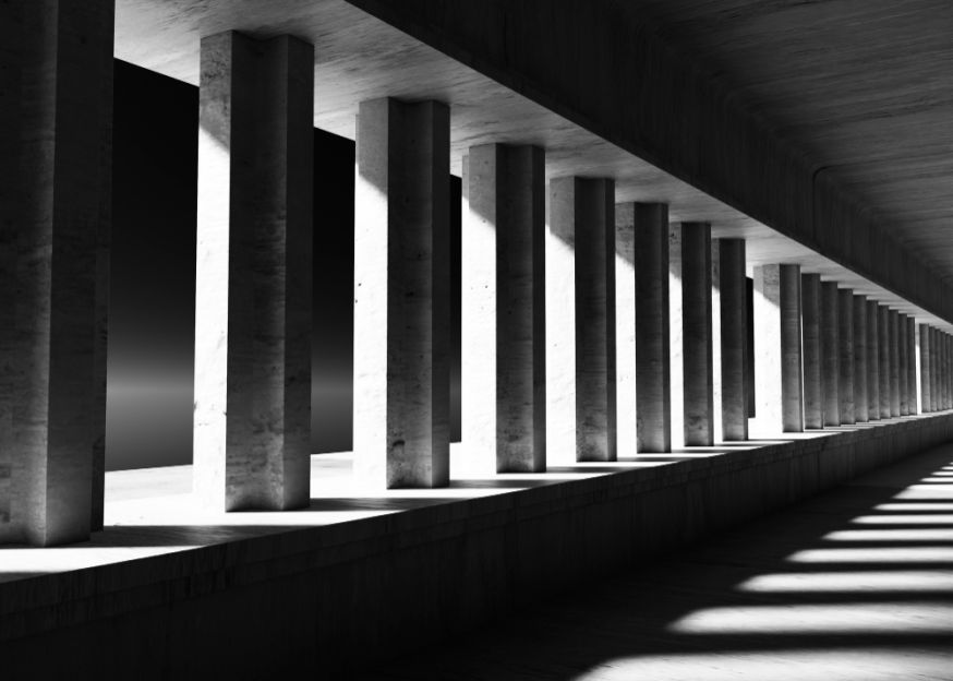 Afbeelding: Een grafische zwart-wit foto van een colonnade waarbij robuuste betonnen zuilen een perfect herhalend verticaal ritme vormen onder een overkapping