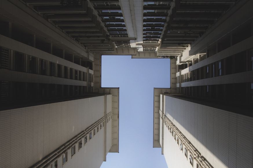 Afbeelding: Architectuurbeeld van onderaf met een vierkante opening naar de lucht en strak symmetrische gevels eromheen