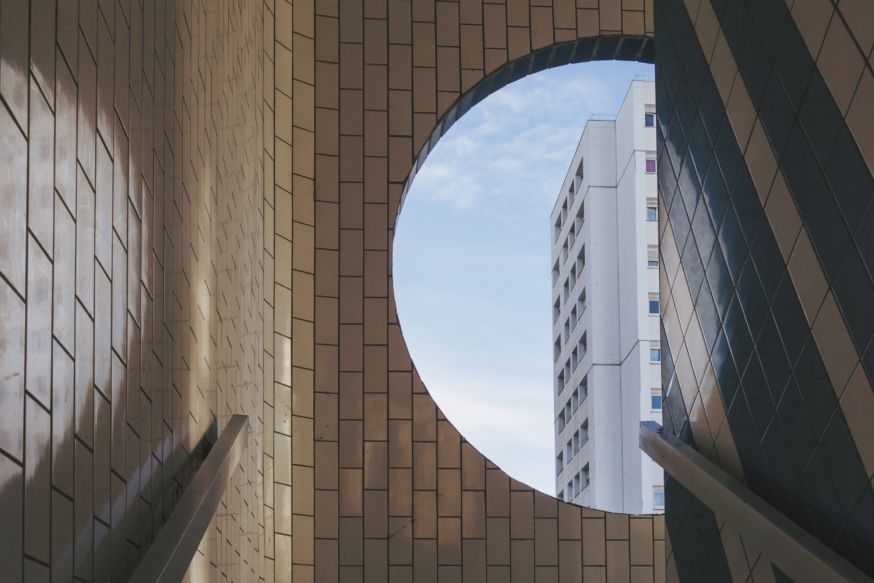 Afbeelding: Ronde opening in architectuur met veel open lucht en een gebouw op de achtergrond