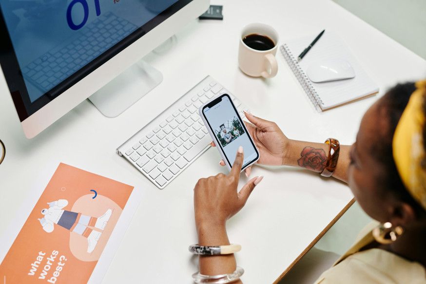 Afbeelding: Bovenaanzicht van een creatieve ondernemer aan een bureau die een foto beoordeelt op haar smartphone, naast een paper met de tekst "what works best?"