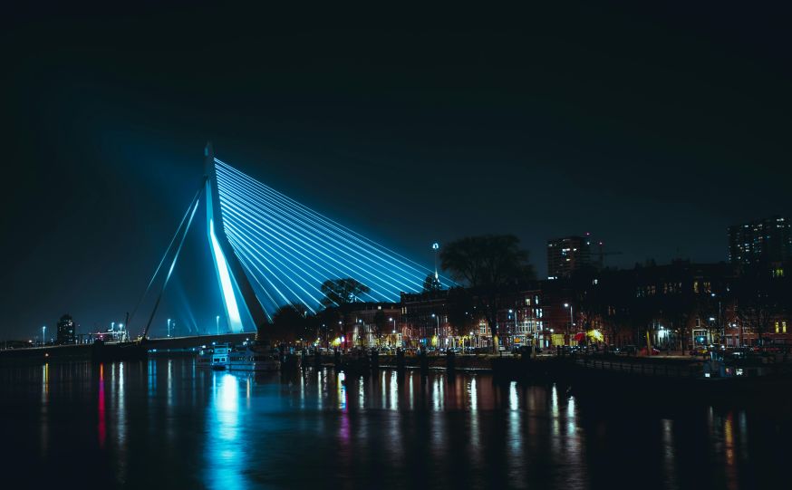 Afbeelding: De iconische, verlichte Erasmusbrug in Rotterdam bij nacht, prachtig weerspiegeld in het water van de Maas