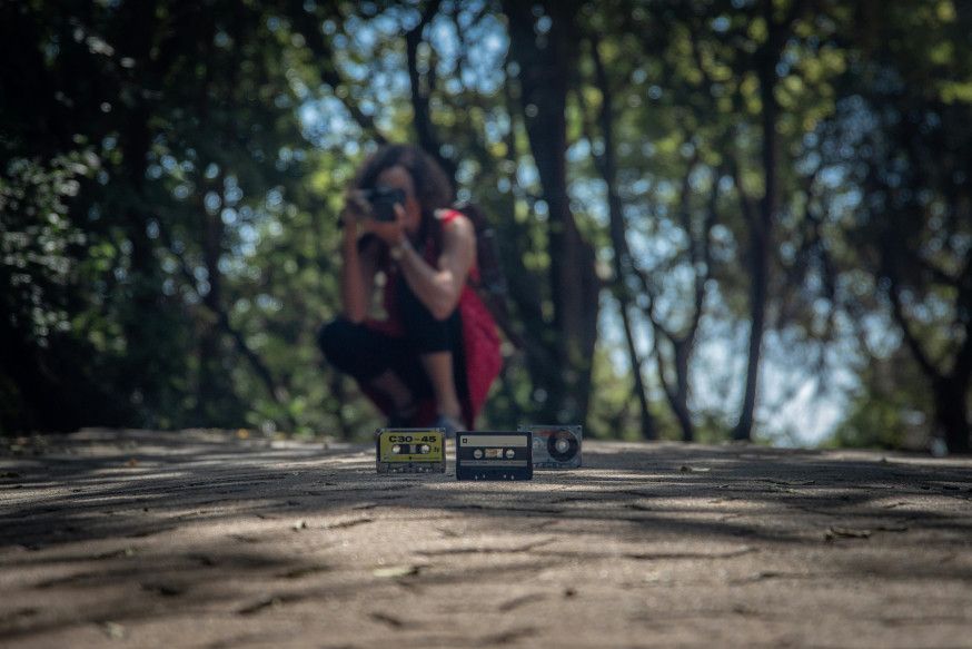 Afbeelding: Fotograaf neemt een laag standpunt in om vintage cassettebandjes op de grond te fotograferen tijdens een fotoproject met beperking